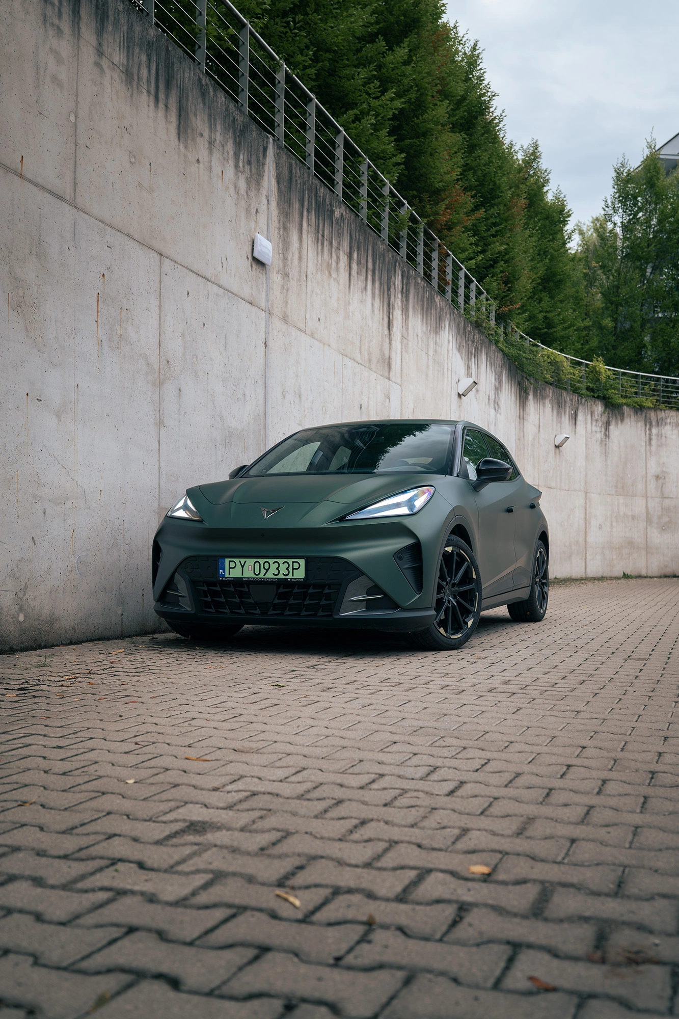 CUPRA Raval w kolorze Manganese Matt na tle minimalistycznego, surowego muru